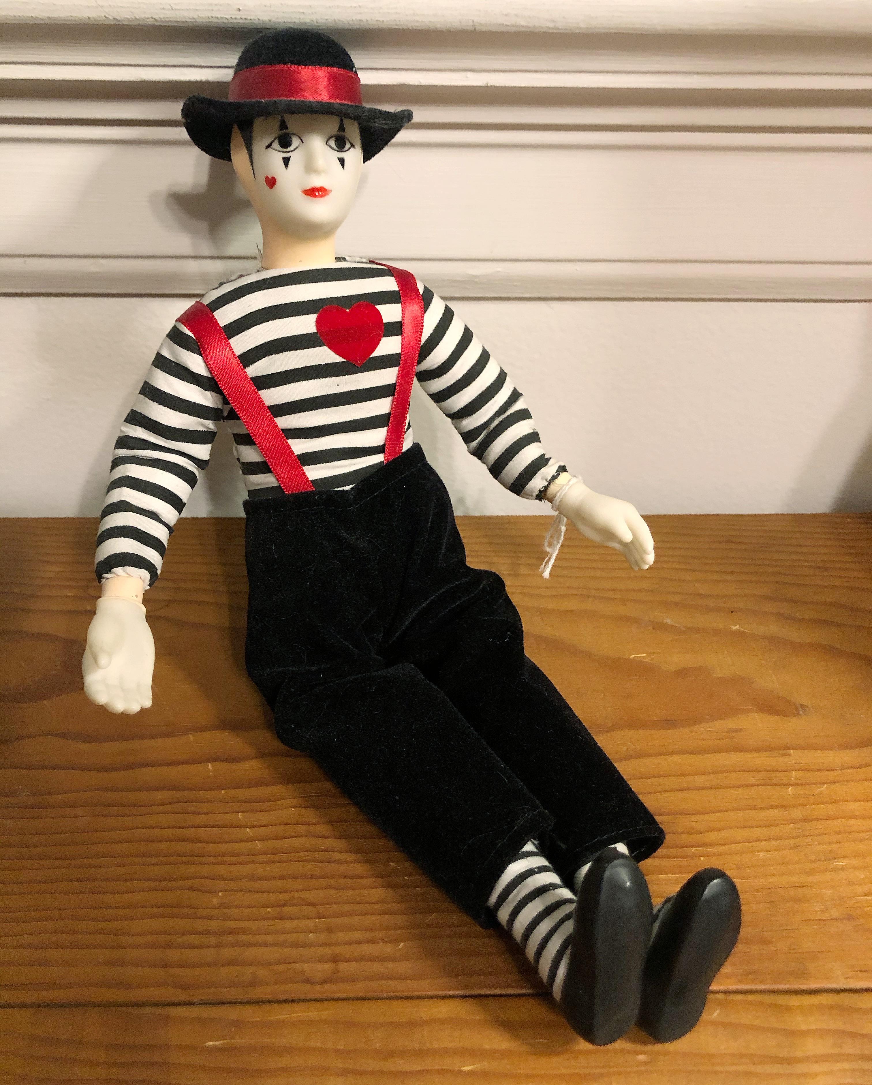 a photo of a fabric mime clown doll with a black and white striped shirt with a small red heart sown on it, black pants with red suspenders and a black hat with a red fabric stripe